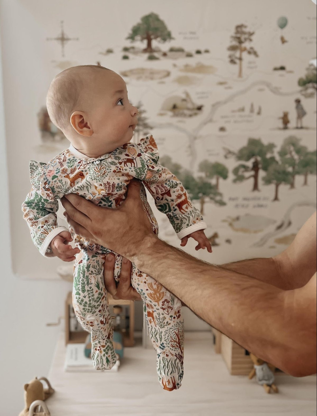Baby in a floral outfit being held with a map on the wall in the background