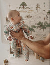 Baby in a floral outfit being held with a map on the wall in the background