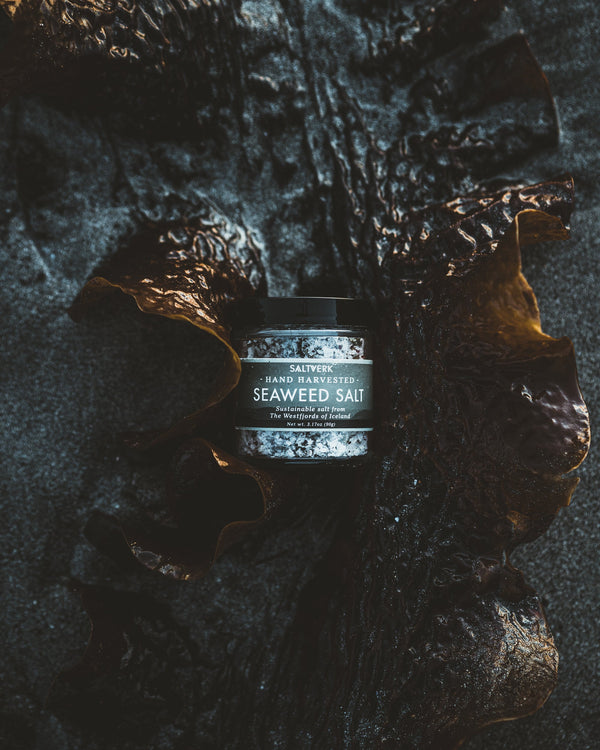 Jar of seaweed salt on a dark, textured surface with seaweed around