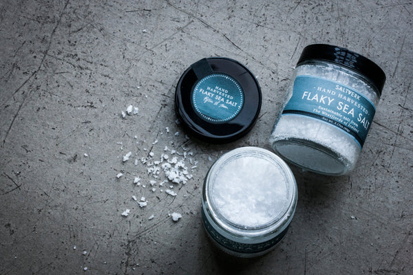 Three jars of flaky sea salt on a textured surface