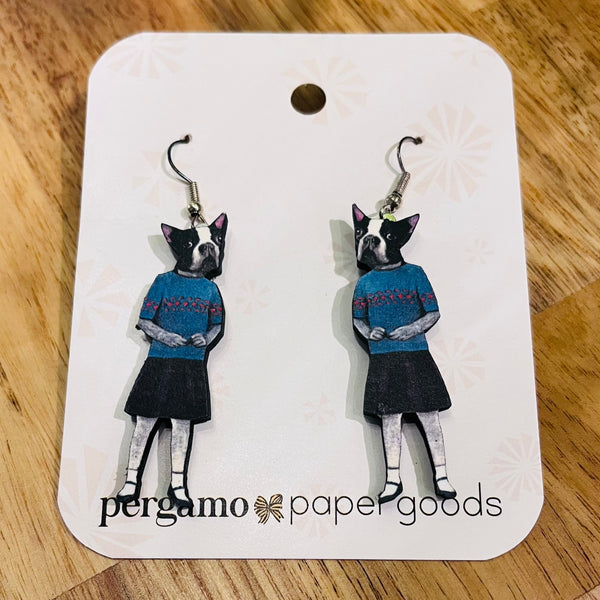 Earrings of a dog wearing a sweater and skirt on a Pergamo Paper Goods card.