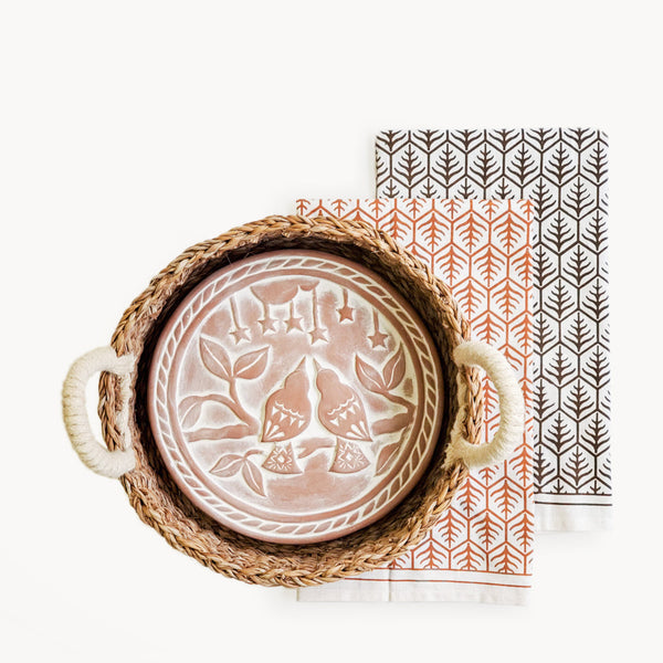 Decorative plate with floral design on a woven tray next to a patterned napkin.