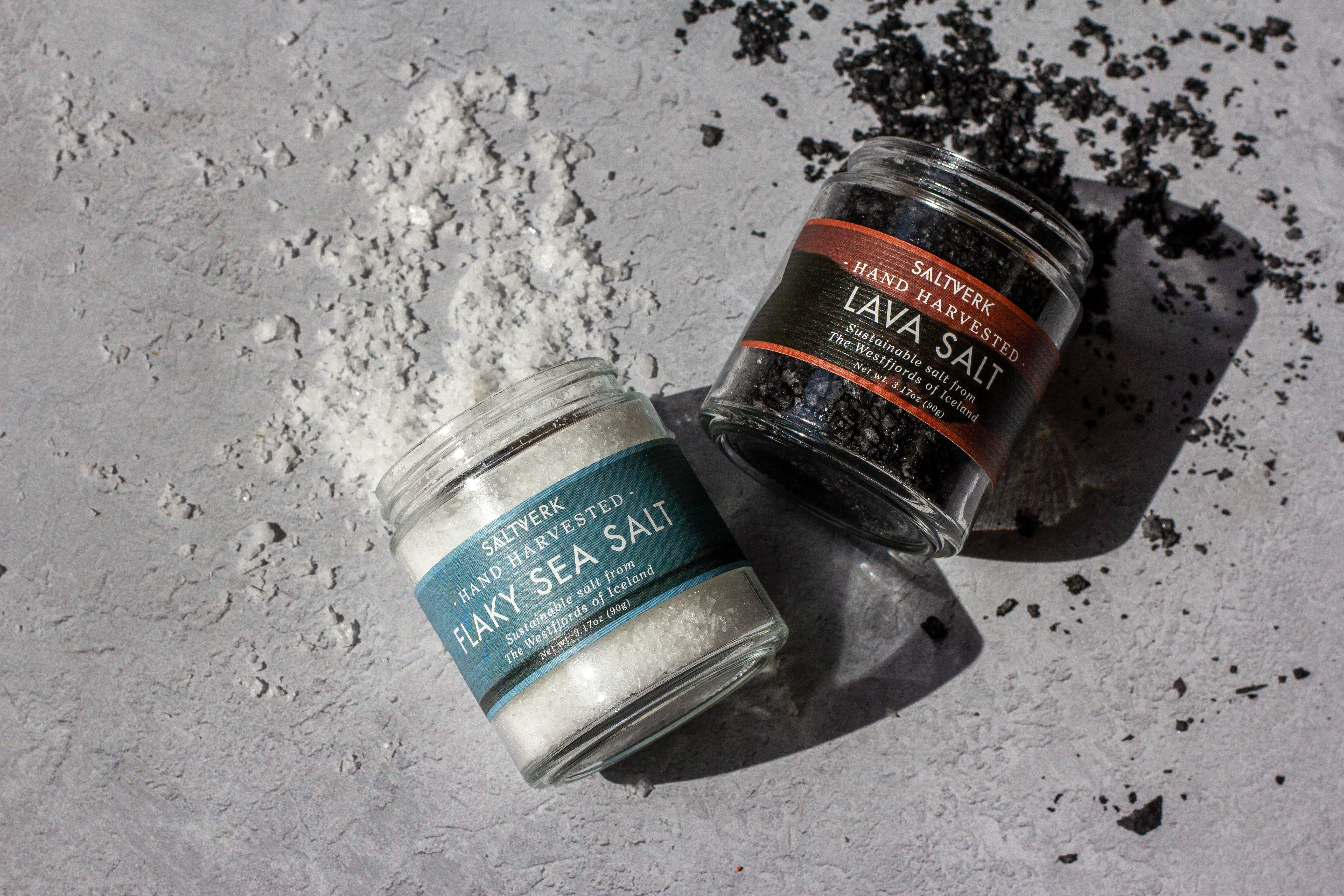 Two jars of Saltwerk salt on a textured surface with scattered salt crystals.