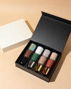 Set of nail polish bottles in various colors displayed in an open black box on a beige background.