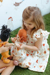 Child holding Apple Park Feathered Friends doll dress showing charming hen illustration print and flutter sleeve detail