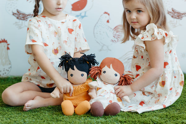 Close-up of Apple Park Feathered Friends doll dress on a soft doll showing the organic cotton fabric and earthy print detail
