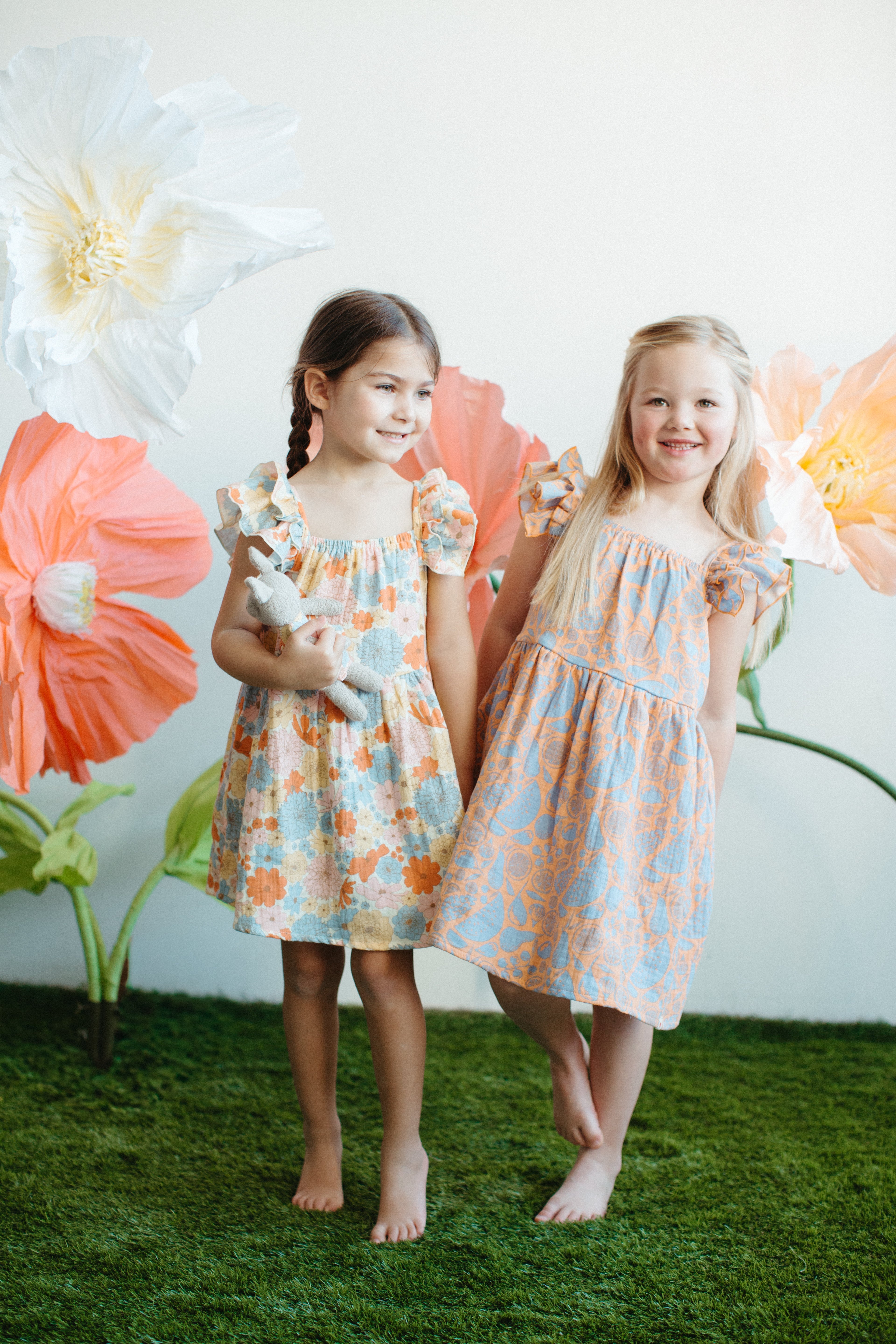 Baby wearing GOTS-certified organic muslin dress with colourful fruit print, sitting outdoors in summer