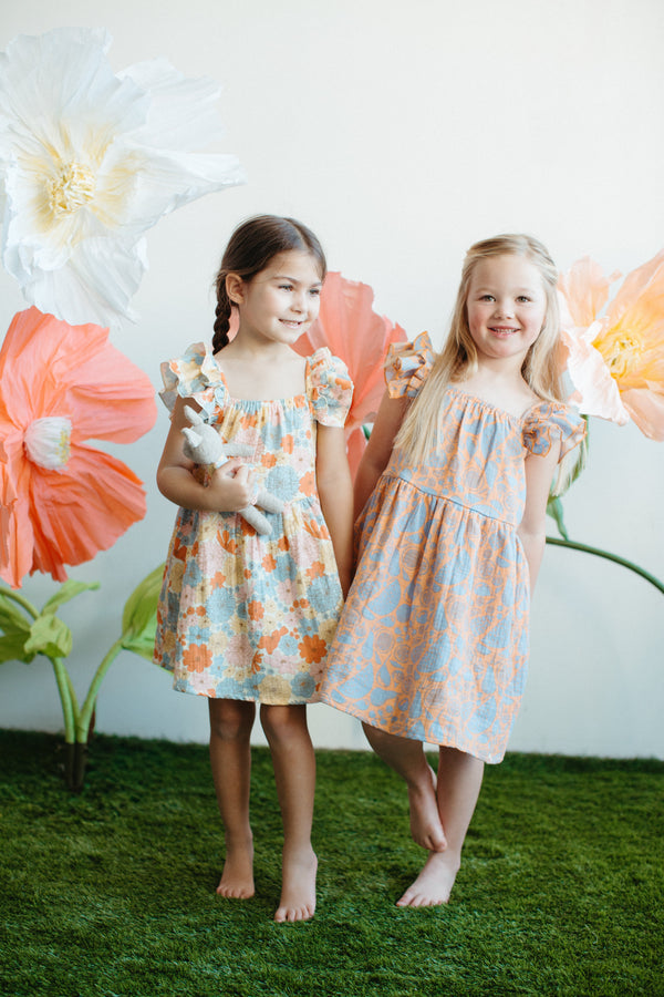 Baby wearing GOTS-certified organic muslin dress with colourful fruit print, sitting outdoors in summer