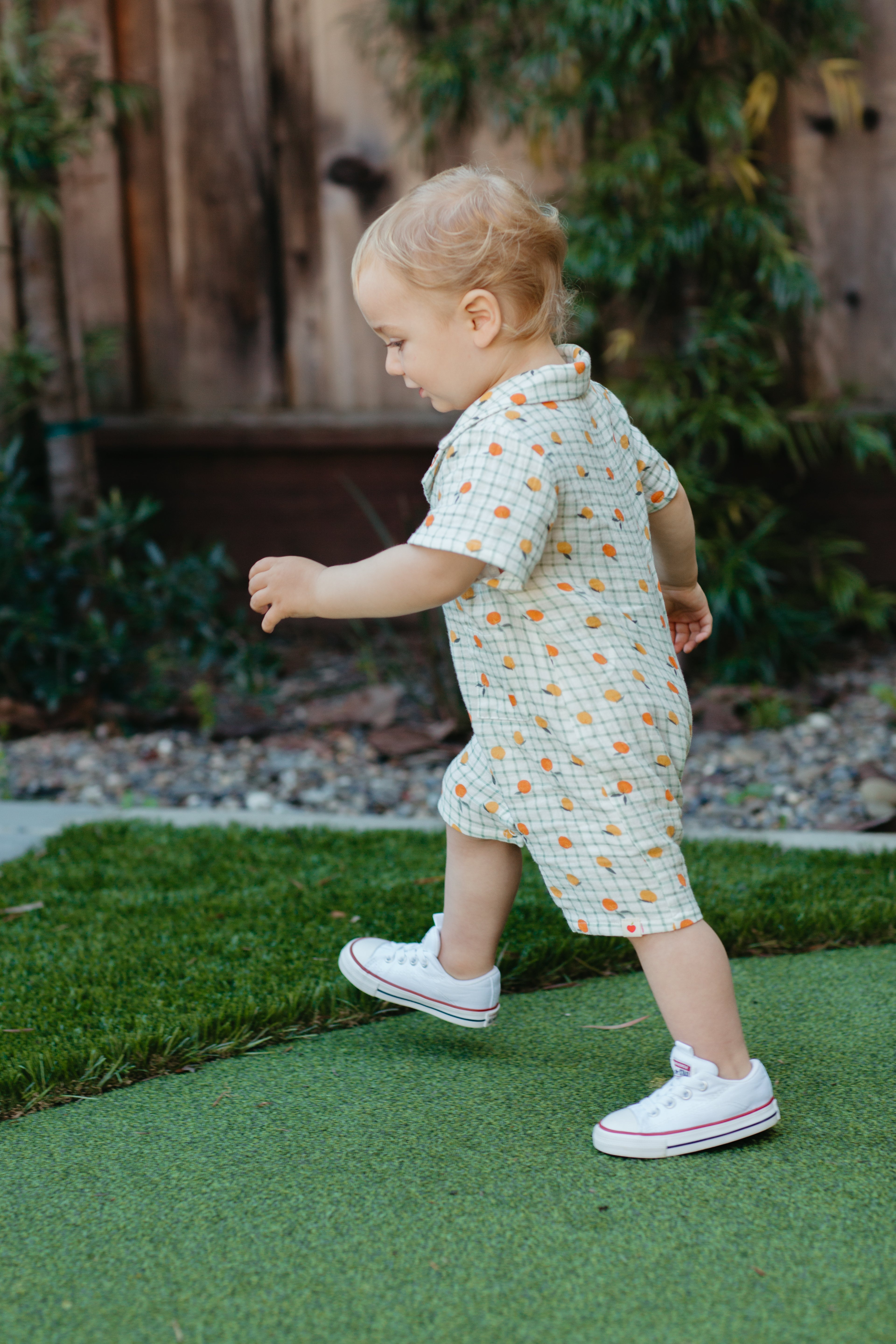 Close-up of Gingham Grove muslin romper showing green gingham print with playful citrus accents