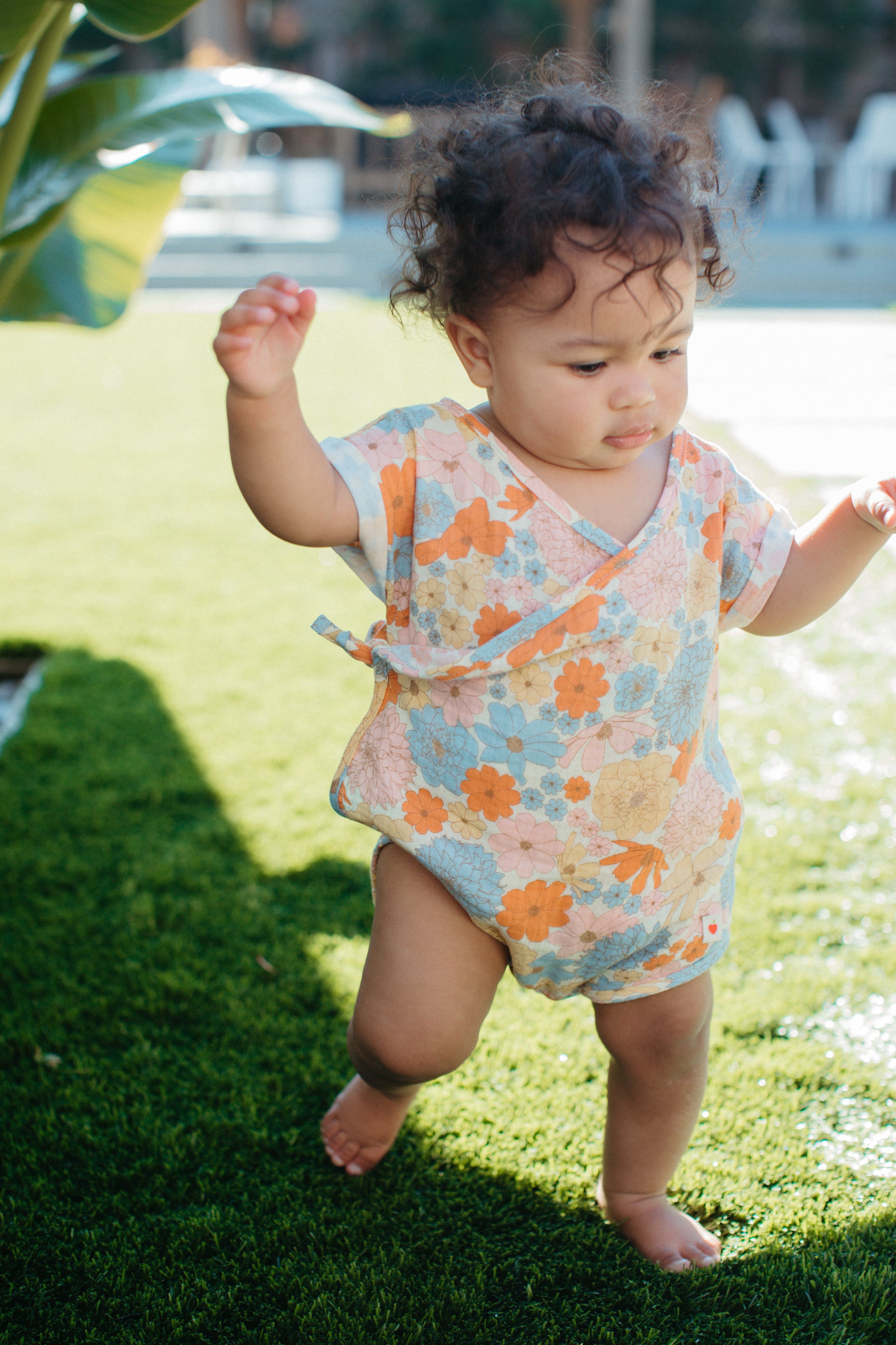 Baby wearing short-sleeve organic muslin romper with vintage wildflower print and wrap-front snap closure
