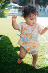Baby wearing short-sleeve organic muslin romper with vintage wildflower print and wrap-front snap closure