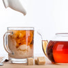 Glass mug with iced tea and lemon, teapot with hot tea, sugar cubes on a wooden surface.