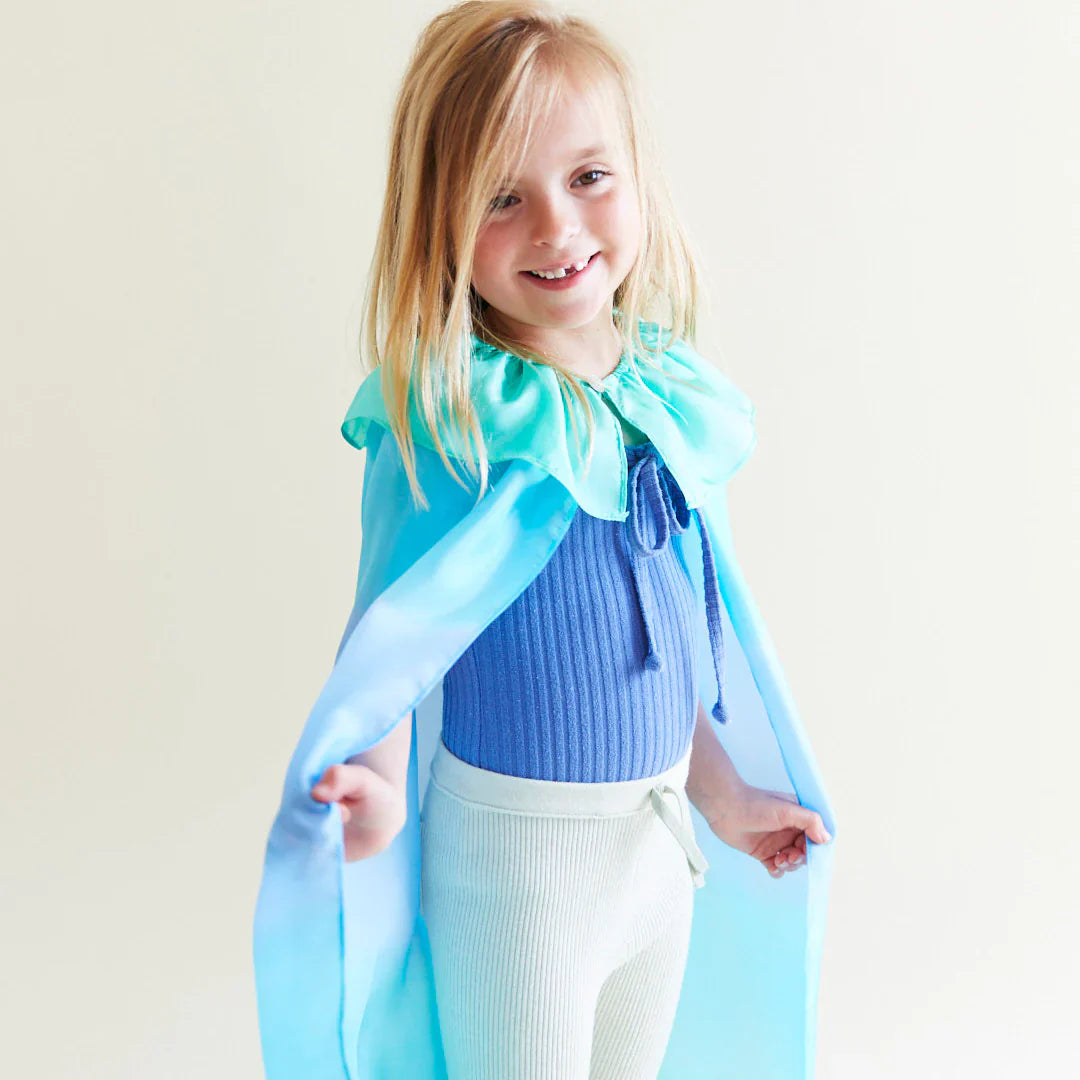 Child wearing a blue cape and smiling against a plain background