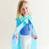 Child wearing a blue cape and smiling against a plain background