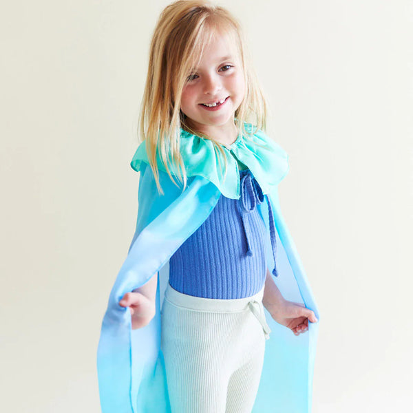 Child wearing a blue cape and smiling against a plain background