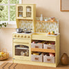 A children's wooden play kitchen in pale yellow, styled in a warm, retro-inspired room. The kitchen features a retro-style oven, a stovetop with gold knobs, a sink with a gold faucet, a floral yellow-and-white patterned backsplash, and three fabric storage bins labeled 'Fruit', 'Bakery', and 'Dishes'.