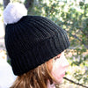 Black knit beanie with a white pom-pom worn by a person outdoors.