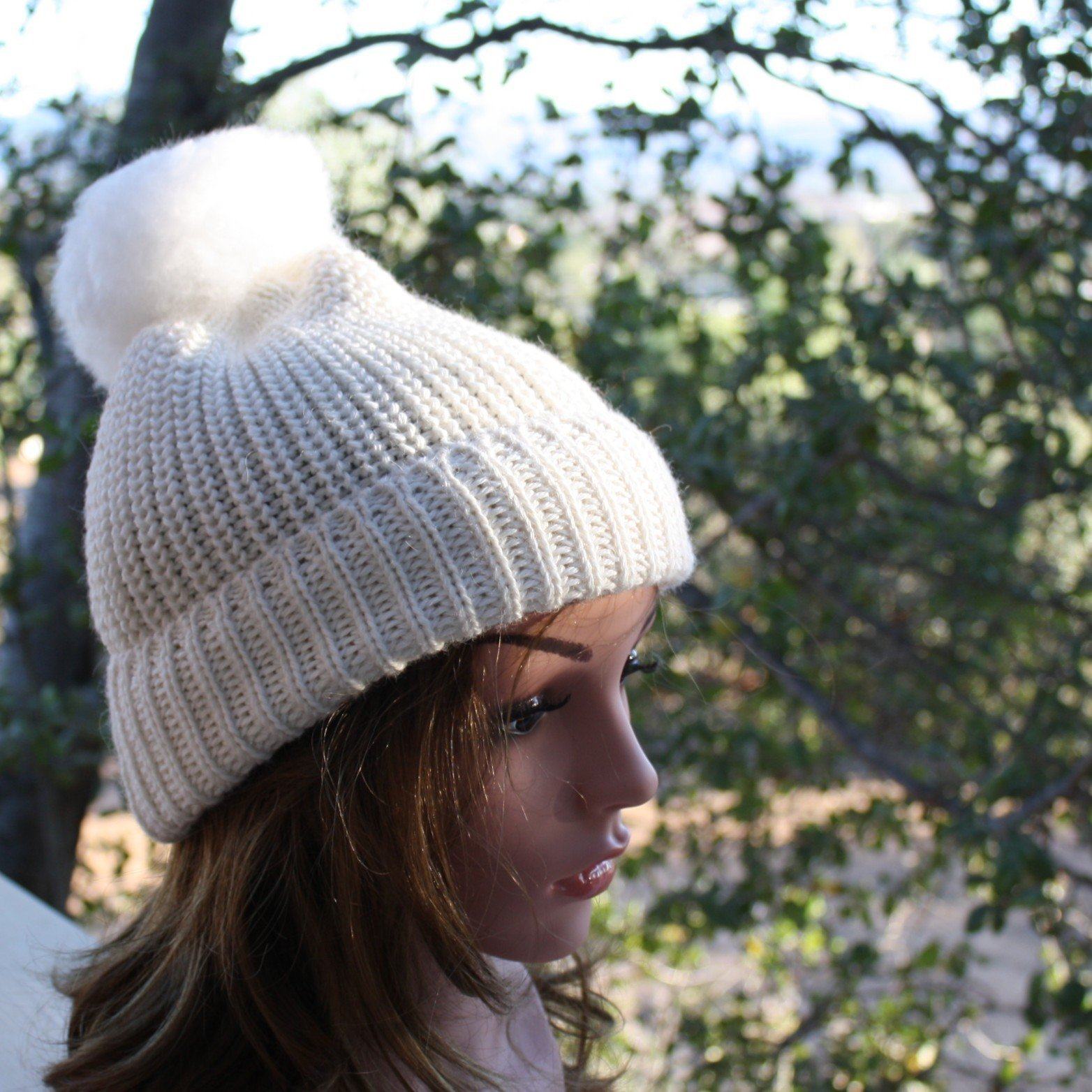 Mannequin head wearing a white knit beanie with a pom-pom against a natural background.