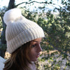 Mannequin head wearing a white knit beanie with a pom-pom against a natural background.
