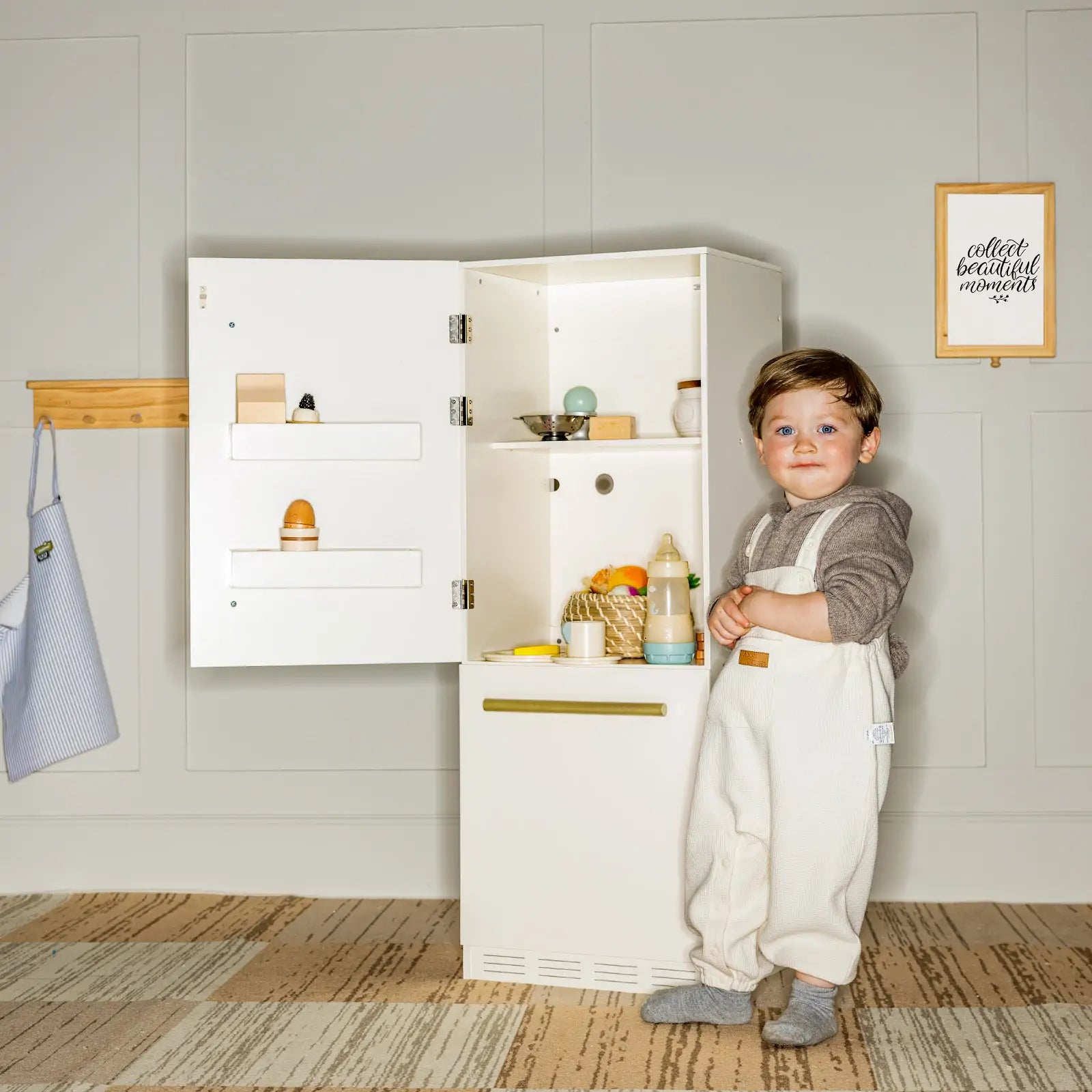Child in a kitchen setting with a toy cabinet and play food items.