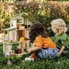 Two children sitting in front of a detailed dollhouse outdoors.