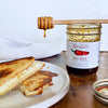 Jar of hot honey with a honey dipper over toast on a wooden table.
