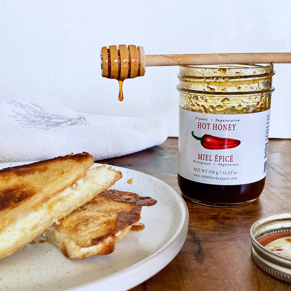 Jar of hot honey with a honey dipper over toast on a wooden table.