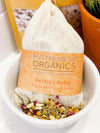Butter Me Up Organics baby bath tea sachet shown with dried organic botanicals including rose petals and lavender buds
