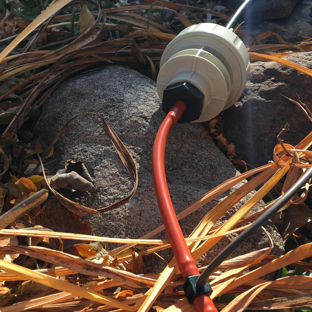 White outdoor electrical plug with red cord on a stone surface with dry leaves.