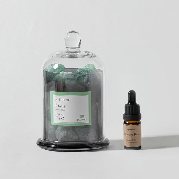 Glass jar labeled 'Sleeping Oasis' with green crystals, next to a dropper bottle on a light gray background.