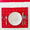 Red patterned placemat with a white plate, fork, knife, and spoon on a white background