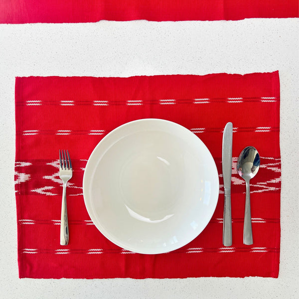 Red patterned placemat with a white plate, fork, knife, and spoon on a white background