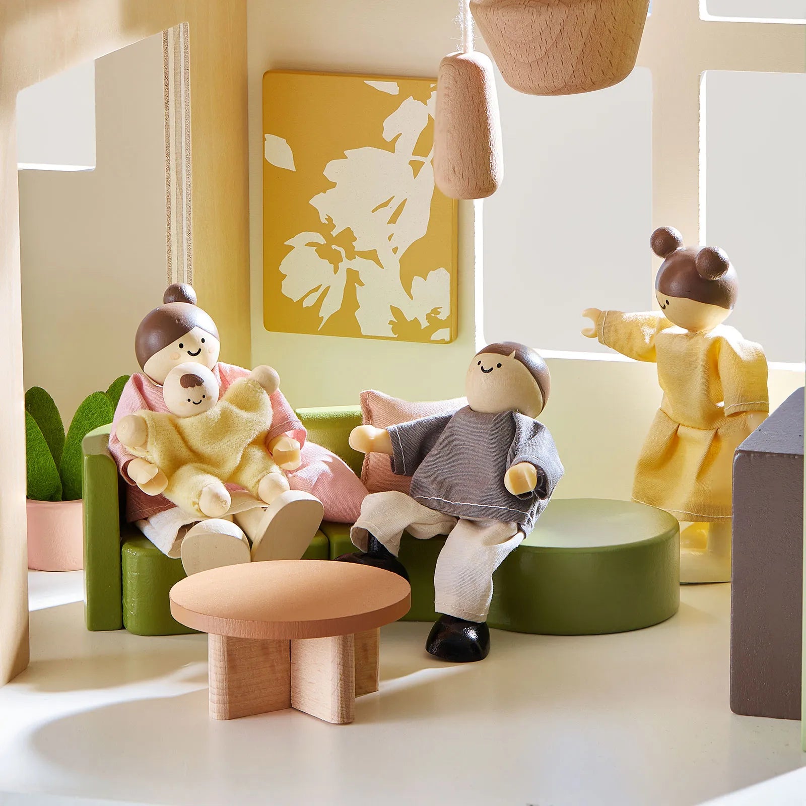 Toy figures of a family in a living room setting with a green sofa, wooden table, and decorative elements.