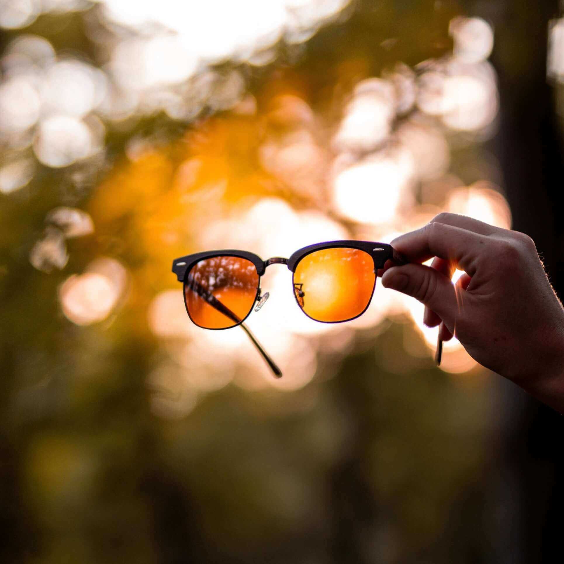 Hand holding a pair of sunglasses with a blurred natural background