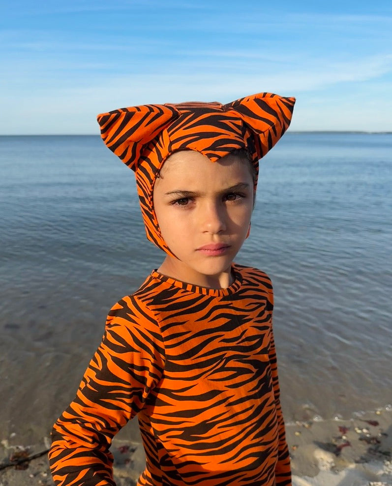 Child wearing a tiger-striped outfit with a headpiece on a beach