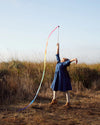 Person in a blue dress holding a colorful hoop in an open field with a clear sky.