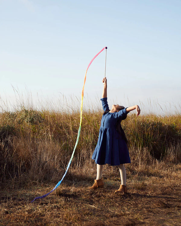 Person in a blue dress holding a colorful hoop in an open field with a clear sky.