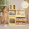 A young girl in a yellow plaid dress plays with a pastel yellow wooden toy kitchen set. The kitchen features a floral patterned backsplash, a sink with a gold faucet, a stove with a glass oven door, and storage bins underneath.