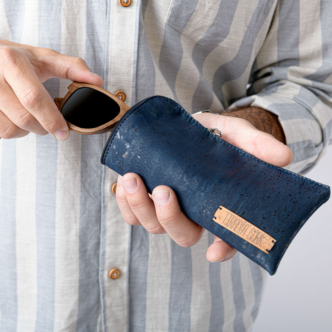 Person holding a navy blue cork eyeglass case with a pair of sunglasses.