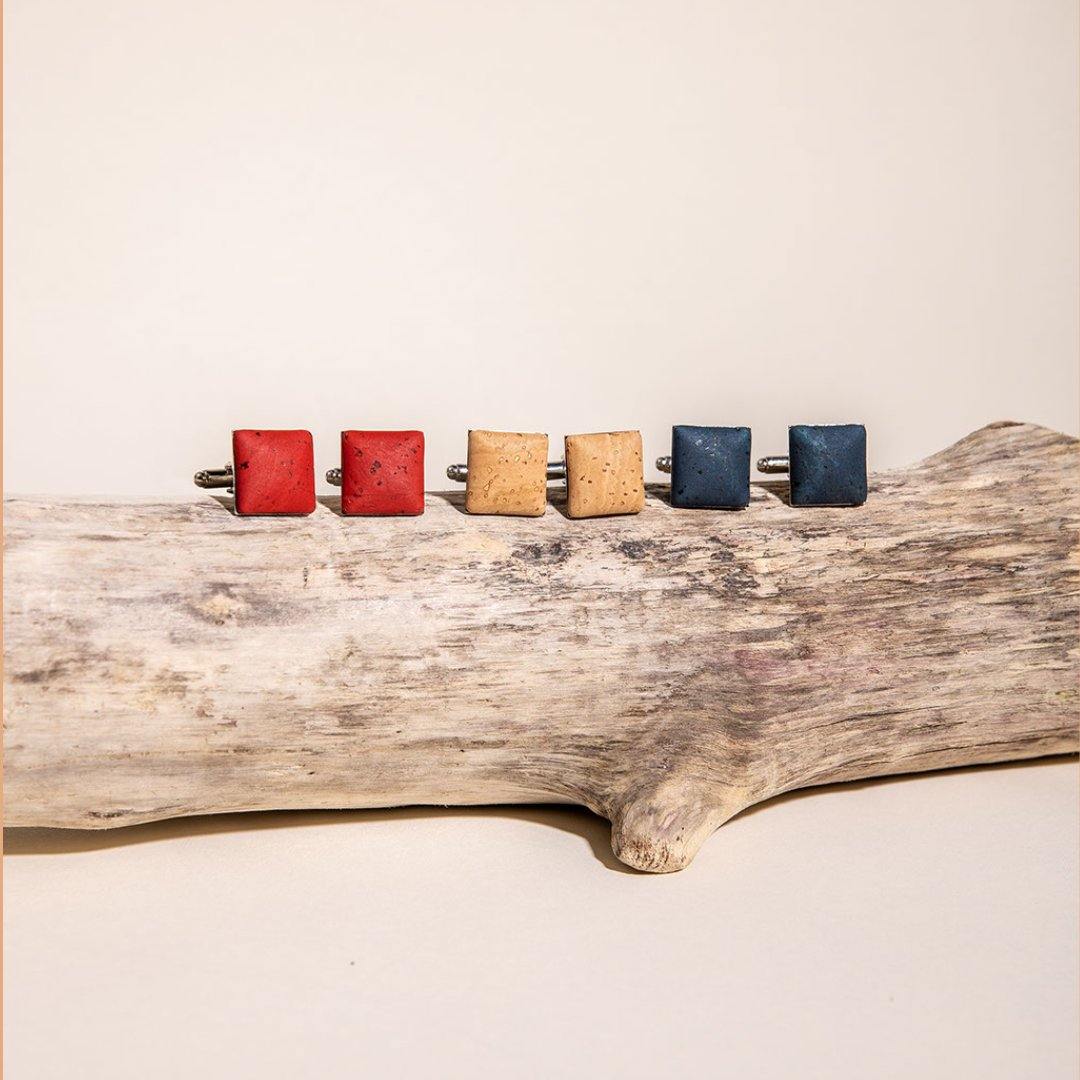 Five square cufflinks in red, brown, and blue on a wooden surface.