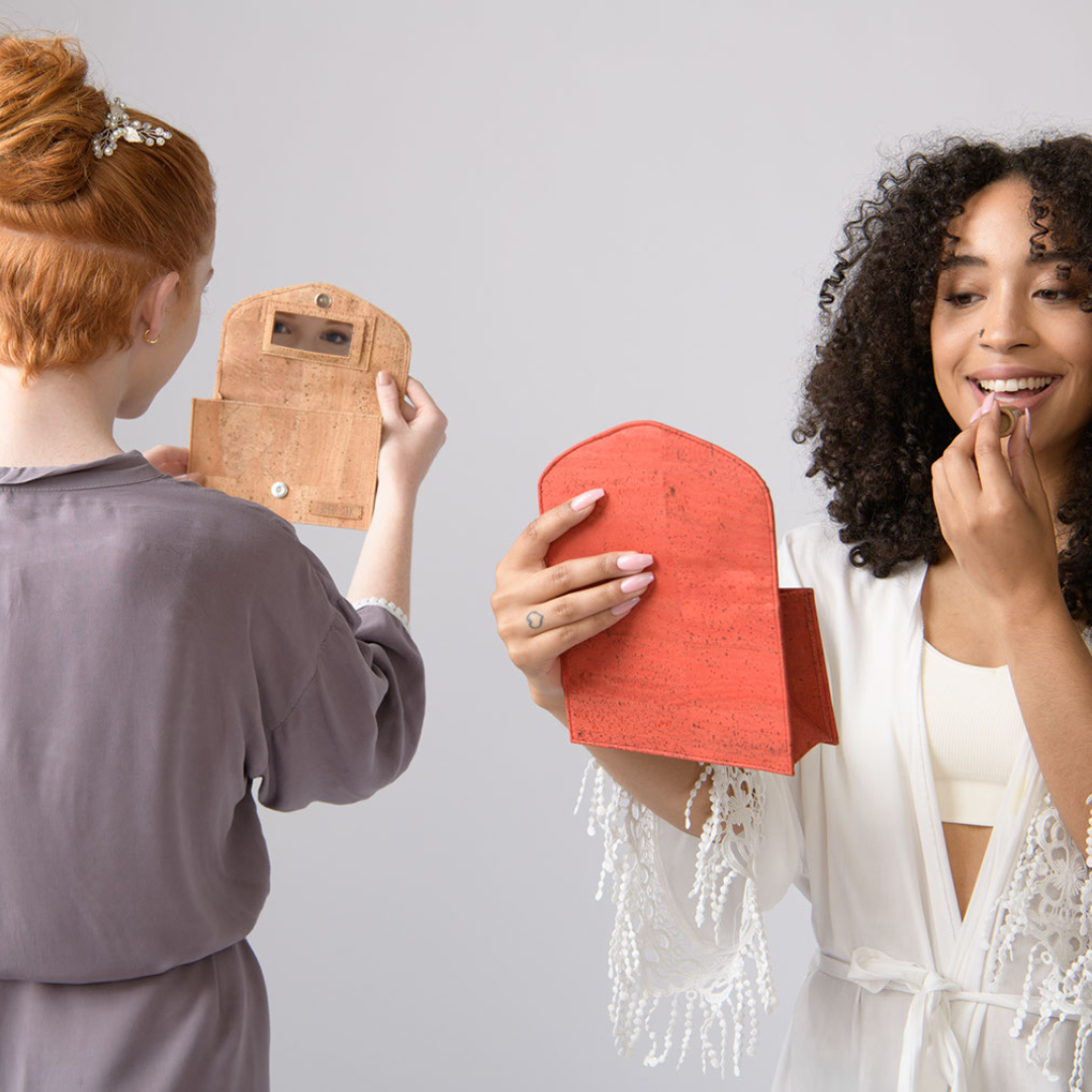 Two women holding small bags, one wooden and one red, against a plain background