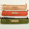 Three cork pencil cases in beige, orange, and green on a white background.