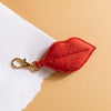 Red leaf-shaped keychain with a gold clasp on a beige and white background