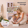 A woman and child are organizing toys in pastel pink Montessori storage boxes on a woven rug, with a matching pink play kitchen in the background. Text reads 'Montessori Storage' and a circular inset highlights the hand-writable label design.