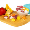 Assorted colorful candies on a wooden board with a strawberry, lemon, and a bowl of candies.