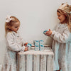 Two young girls in matching outfits standing behind a wooden crate with boxes on it.