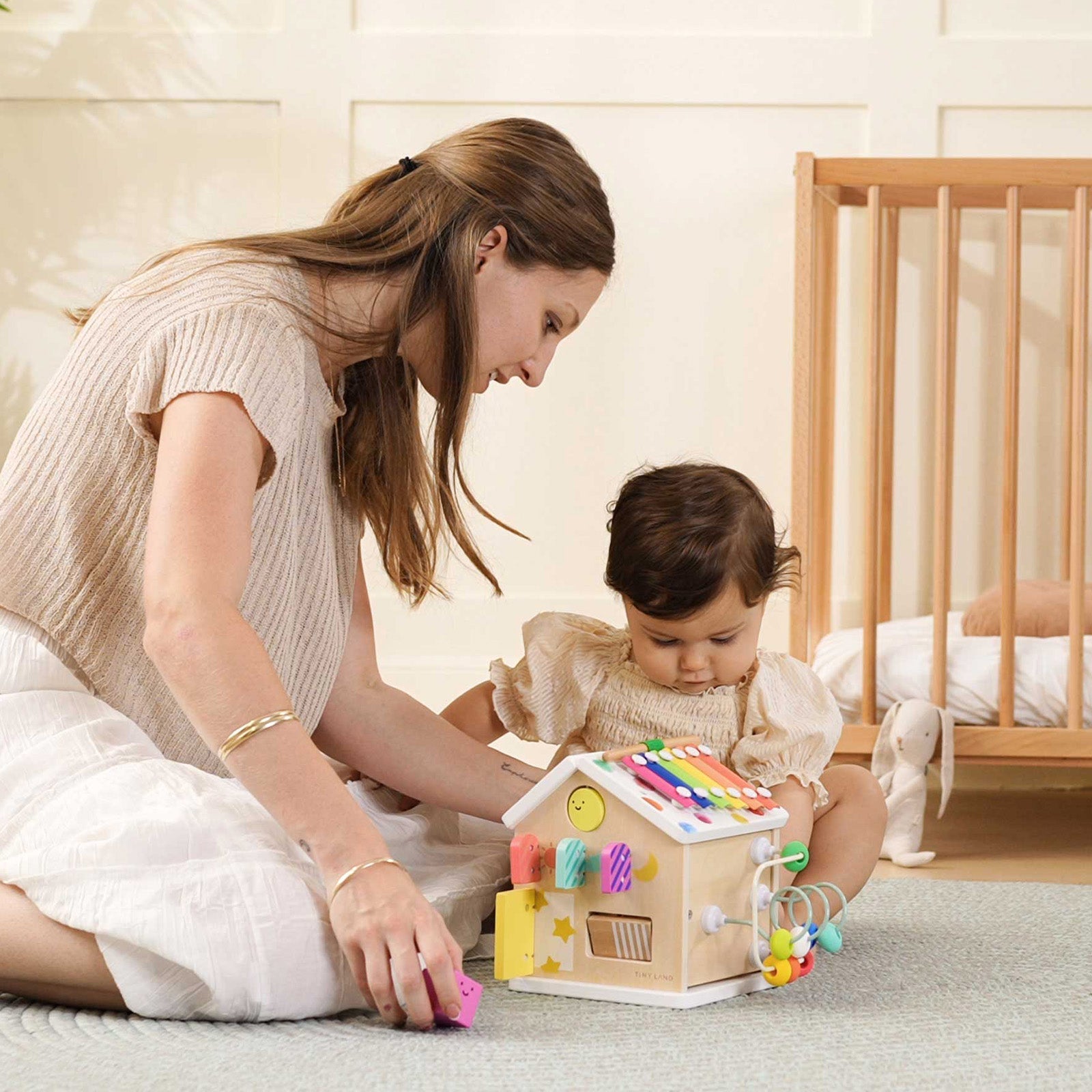 Woman and child playing with a colorful wooden toy house in a nursery.