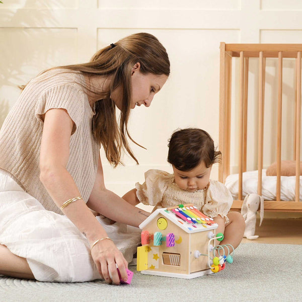 Woman and child playing with a colorful wooden toy house in a nursery.
