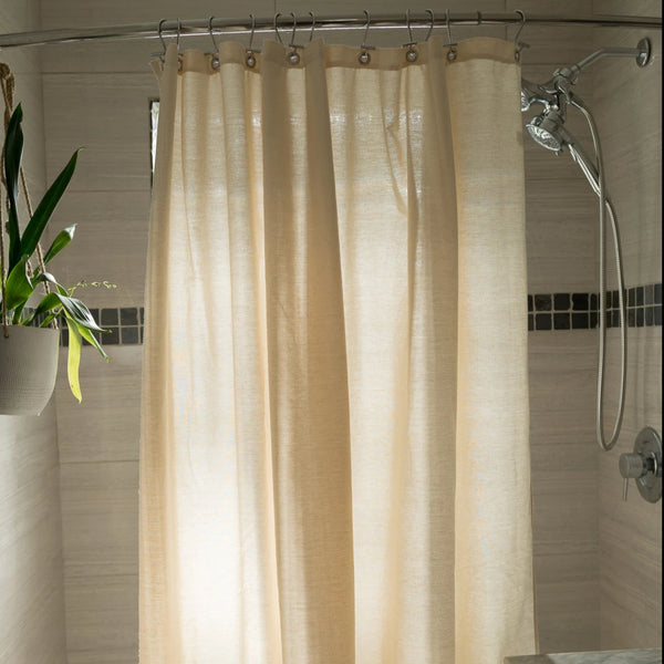 Beige shower curtain in a bathroom with a plant and tiled wall.