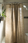 Beige textured shower curtain in a bathroom setting with a plant and light fixture.